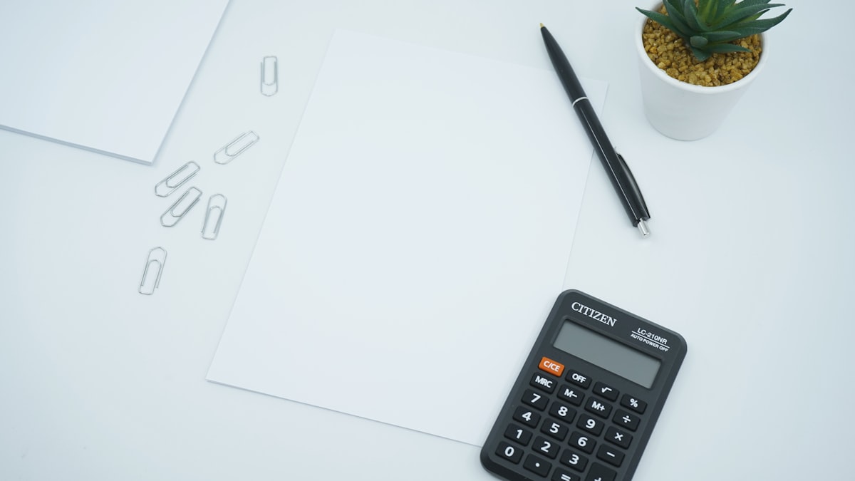 calculadora negra junto a un bolígrafo negro sobre papel de impresora blanco